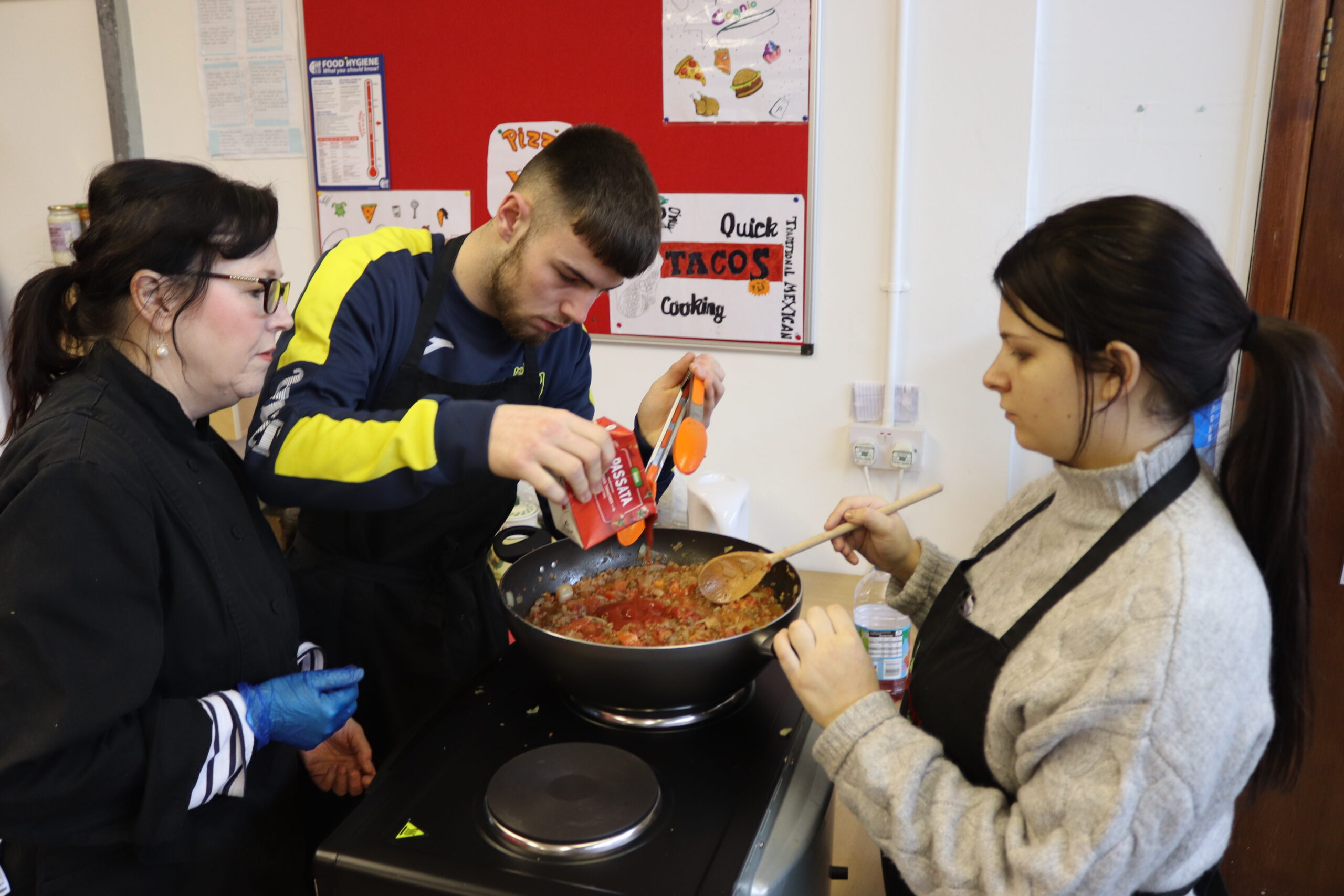 2 hospitality learners and tutor cooking a meal